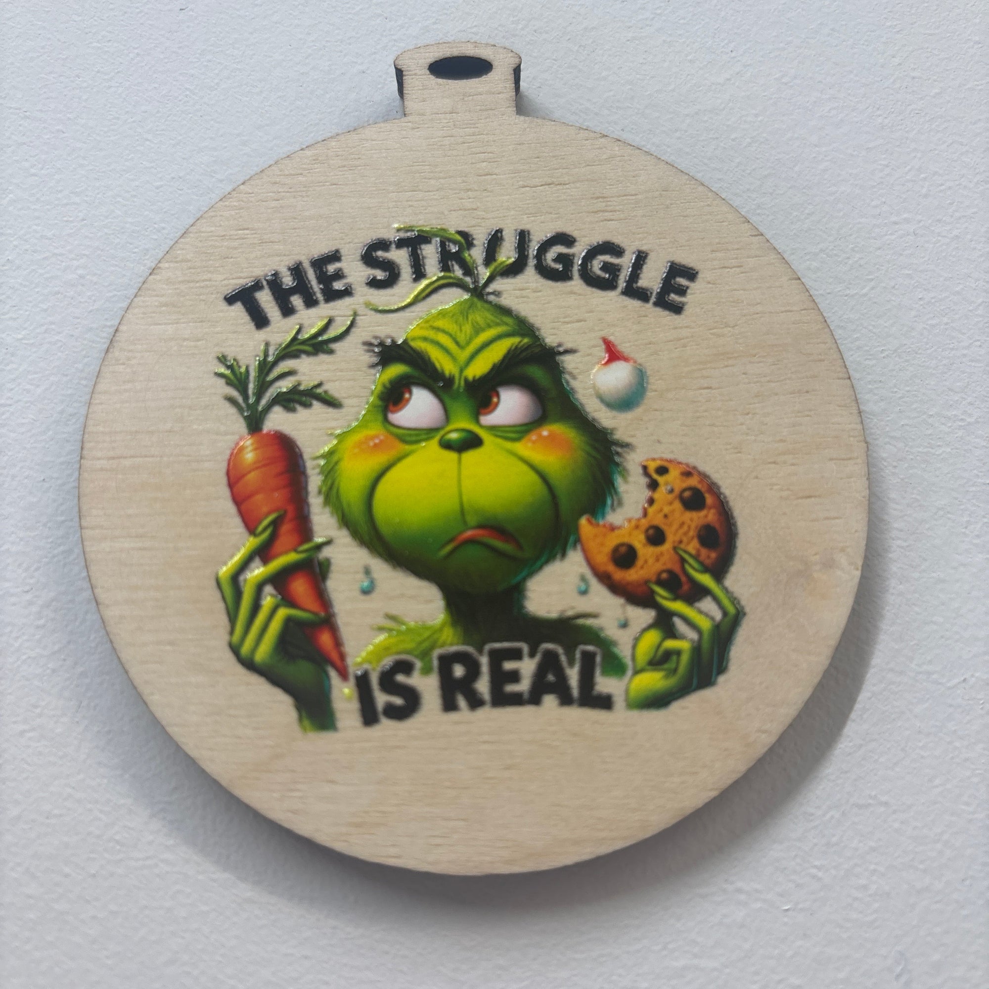 Round wooden sign with a cartoon character and 'The Struggle is Real' text on a white background